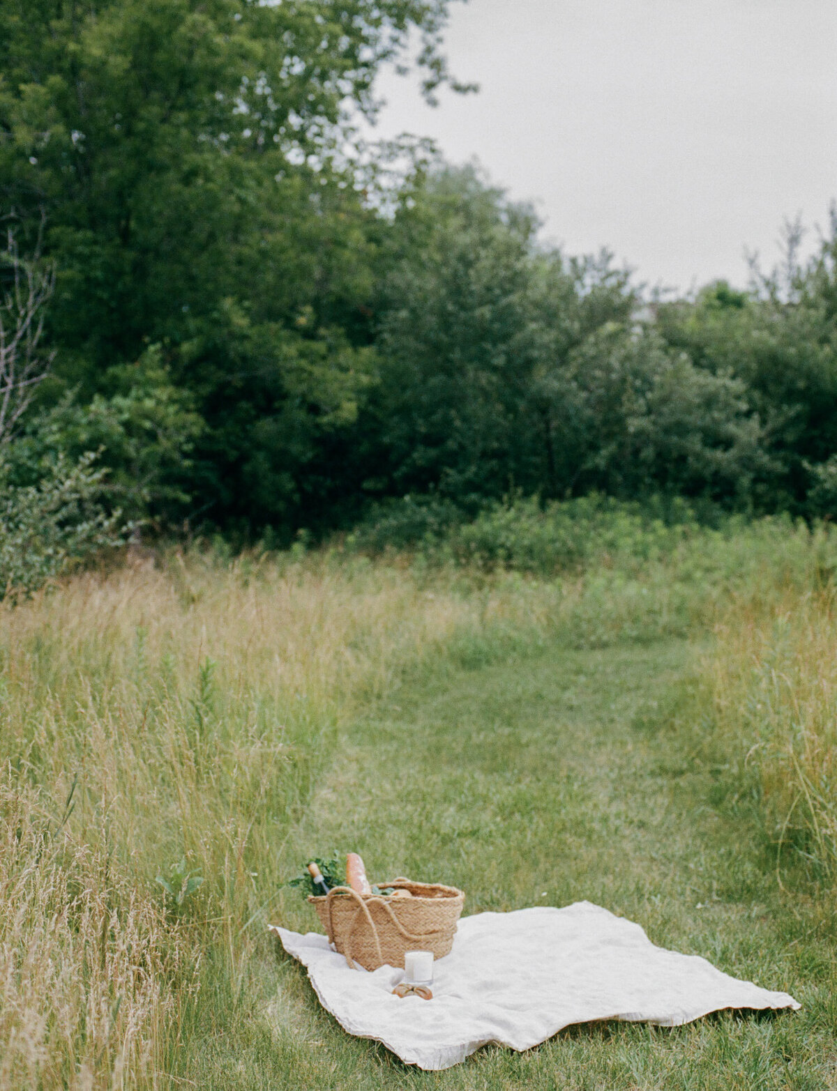 meadow picnic in summer with straw tote, baguette, Detroit Rose Smoked Tomato candle