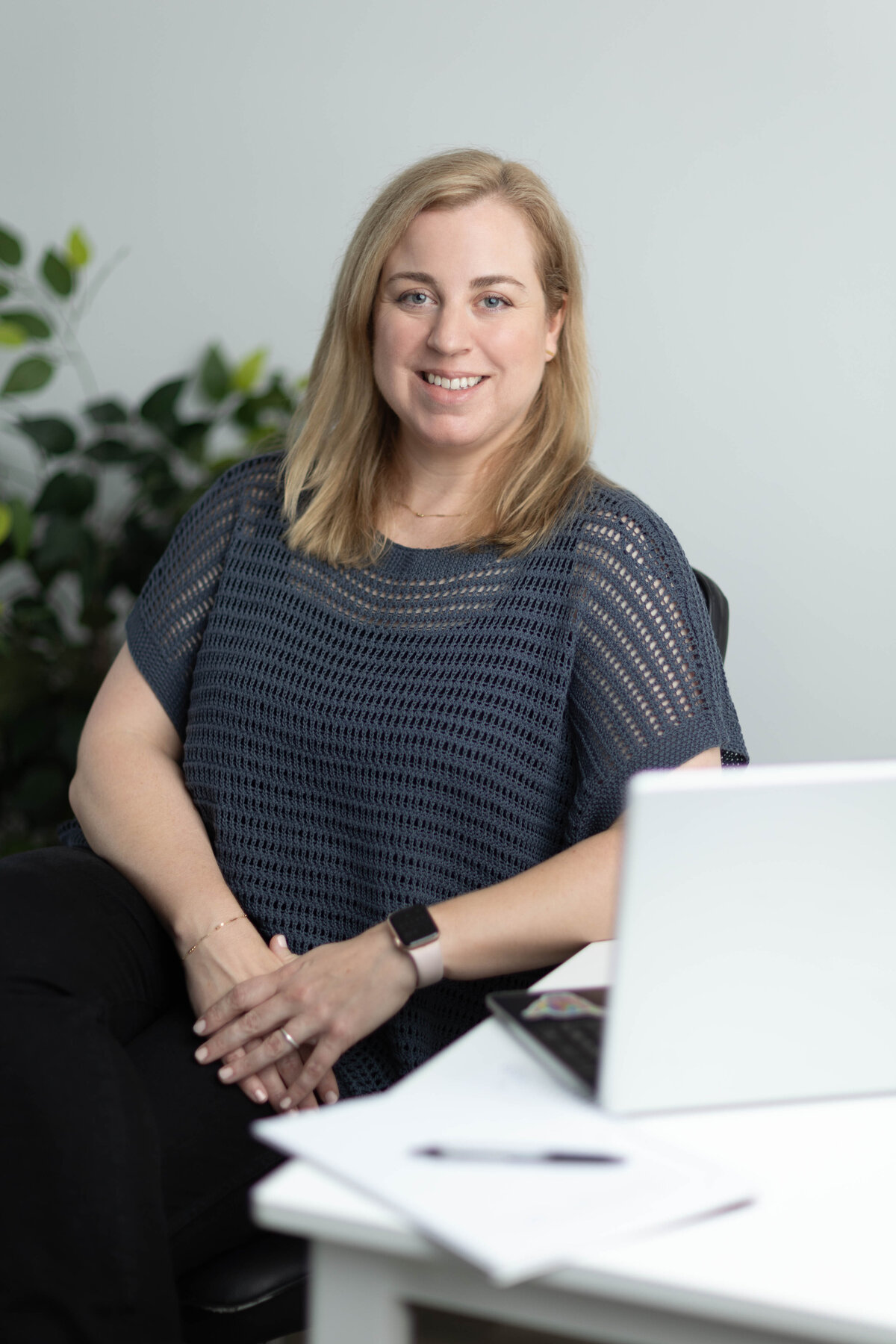 Therapist portrait at desk with laptop and plant in the background