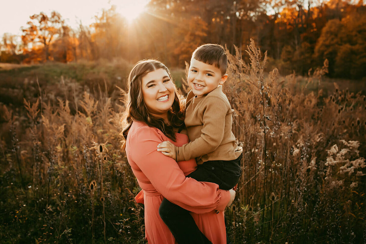 a gorgeous shot of a mom holding her little boy in a field at sunset