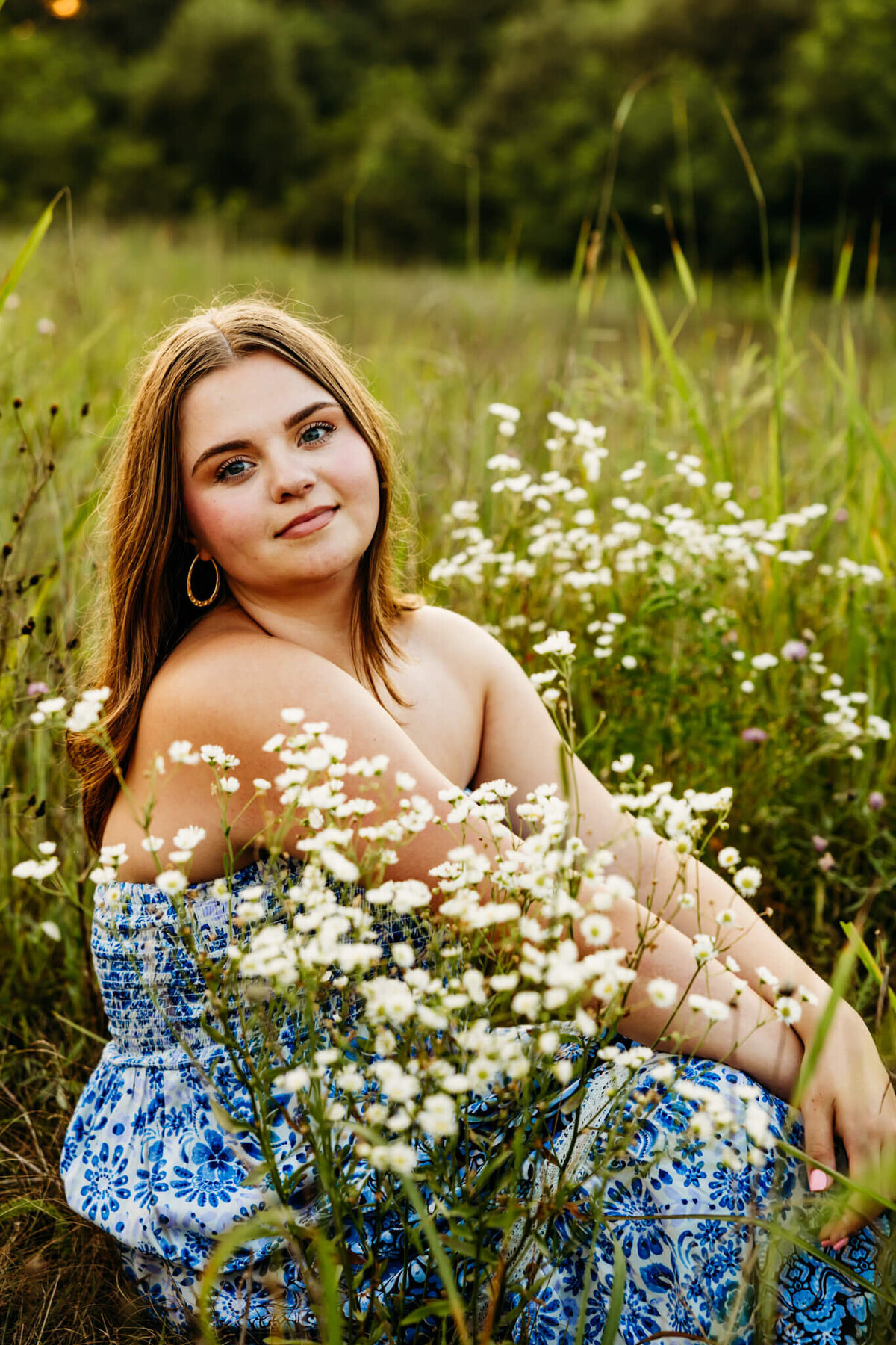 stunning teen girl with short brown hair sitting in between small flowers and glancing over her shoulder for her senior photography session.