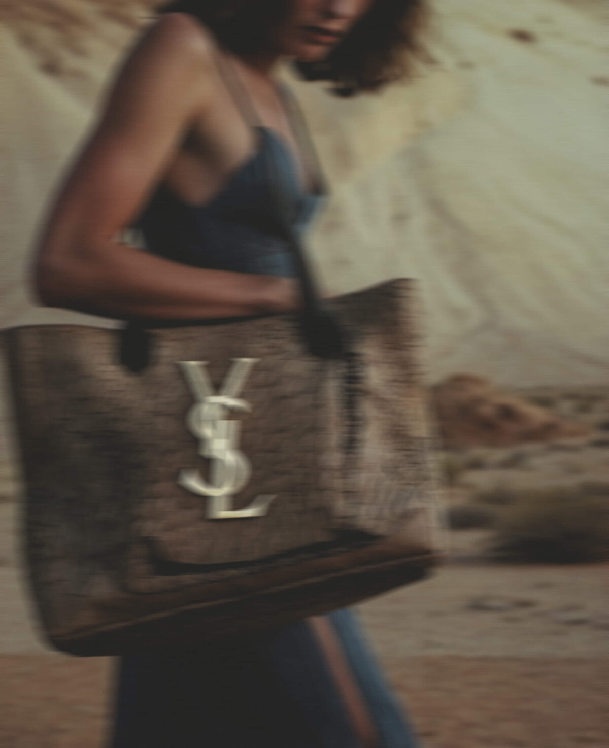 A person in a sleeveless dress holds a large bag with an "YSL" logo, embodying the elegance of Sweet Pea Ink Creative's brand identity in an outdoor setting.