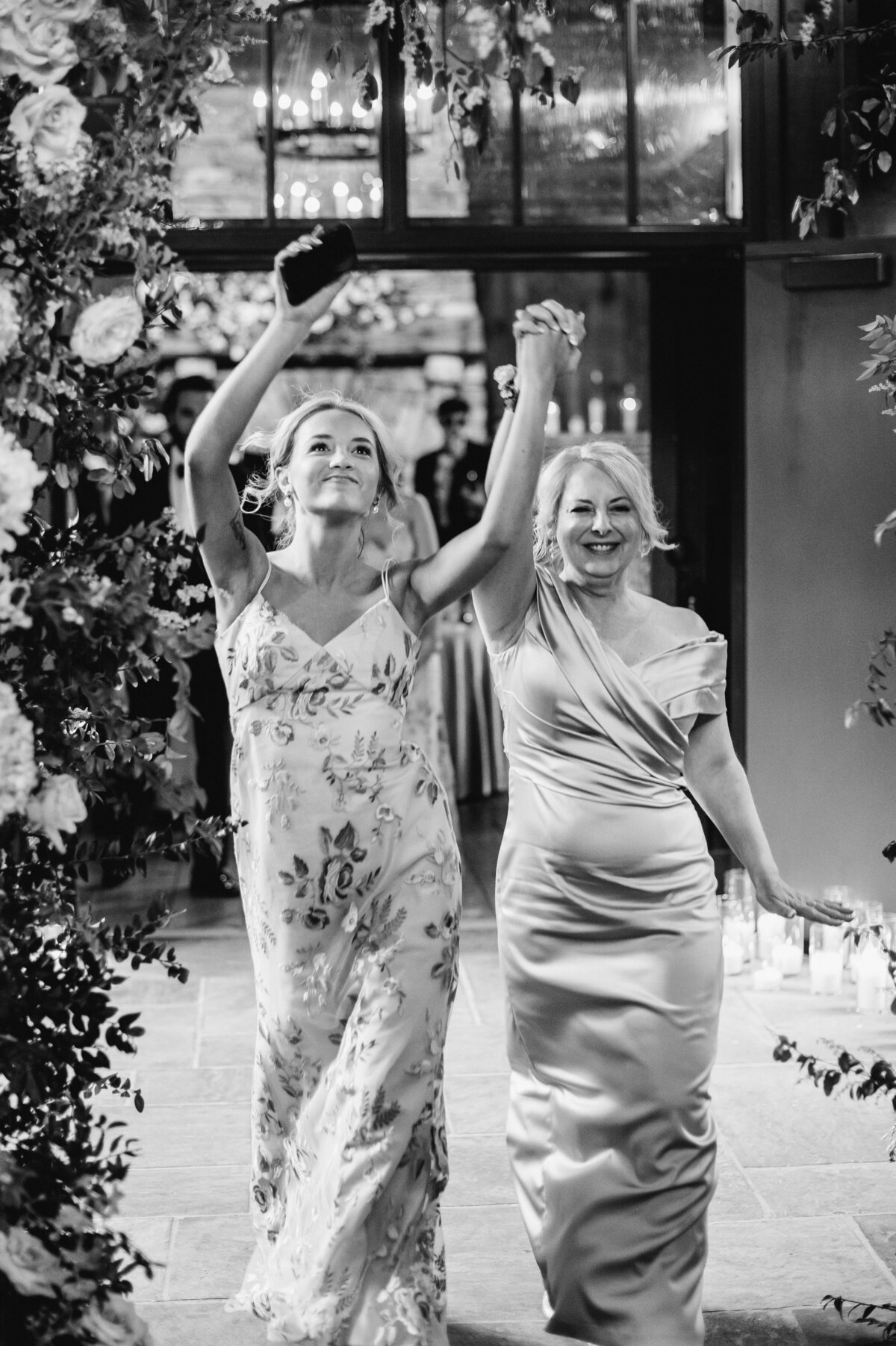 Black and white photo of wedding party members entering the reception under a floral arch at Old Edwards Inn in Highlands, North Carolina.
