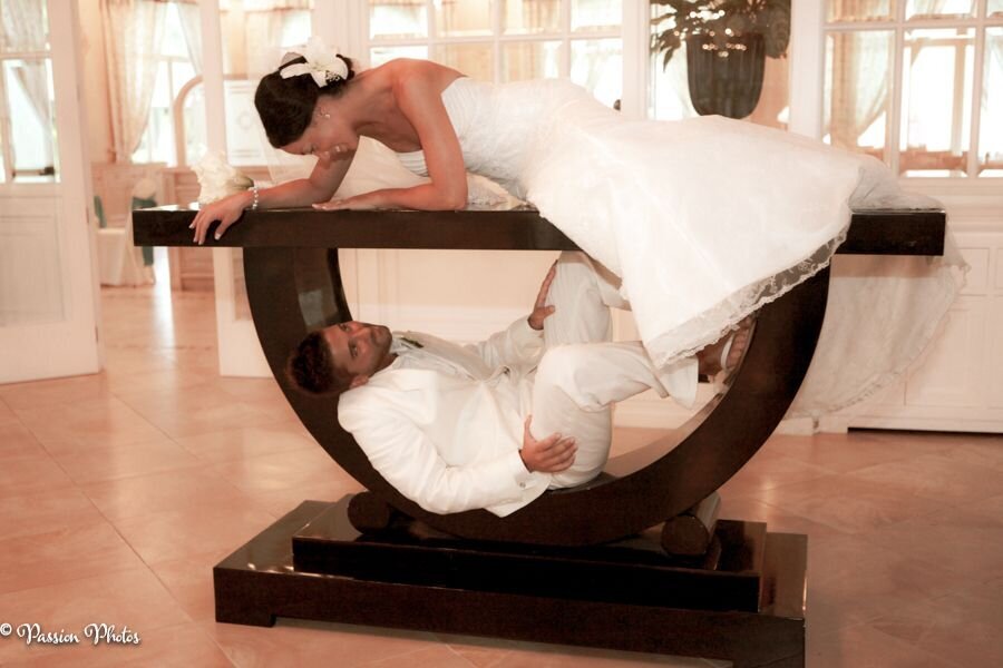 A bride lies playfully on a table, gazing down at her groom, who peeks up from underneath the table. This whimsical and intimate moment captures the fun and unique aspects of destination weddings, showcasing our ability to capture creative and memorable interactions between couples in stunning settings.