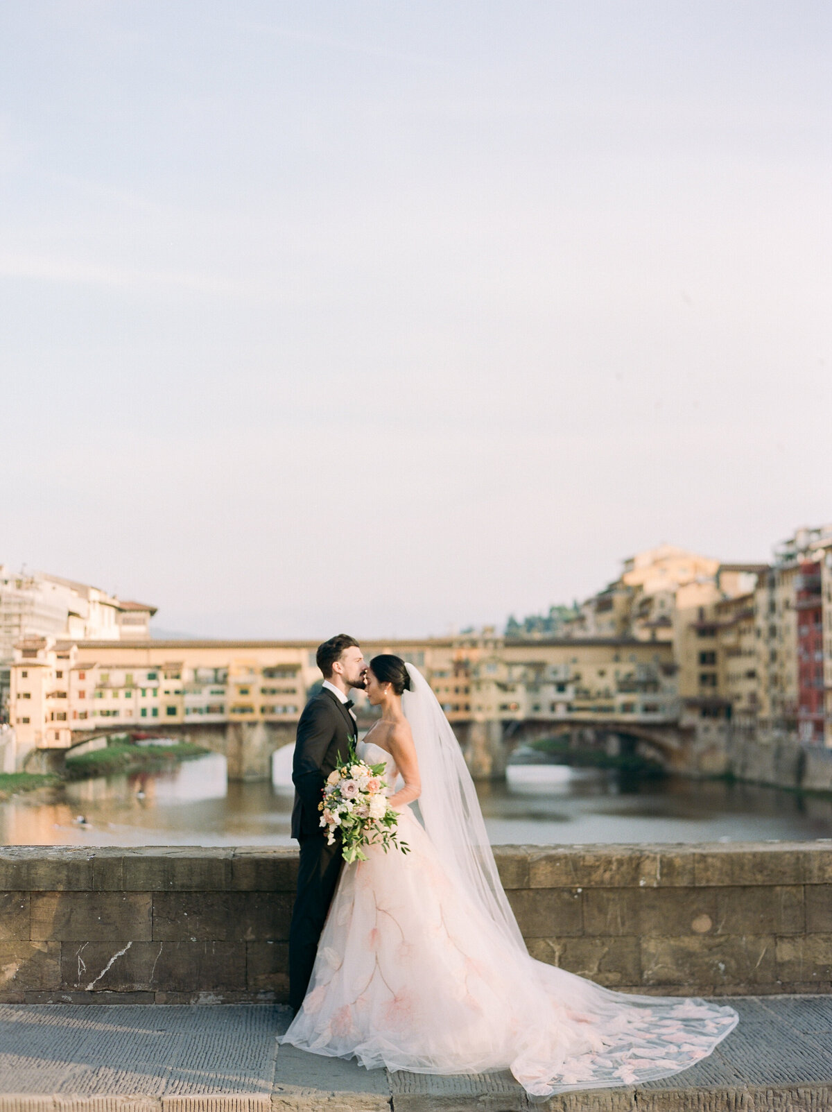 a groom kissing his bride on a bridge in florence italy during sunset