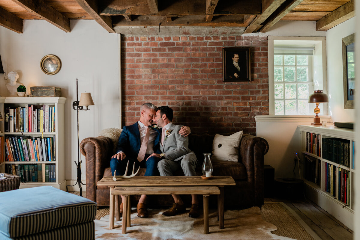 Two grooms sit on the sofa of their private estate while gazing into each other's eyes