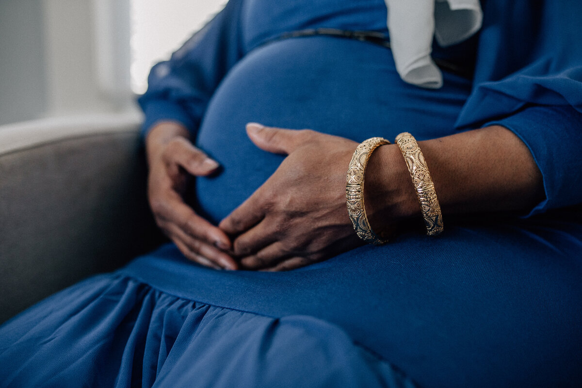 Pregnant woman sits ina. chair and holds her belly.