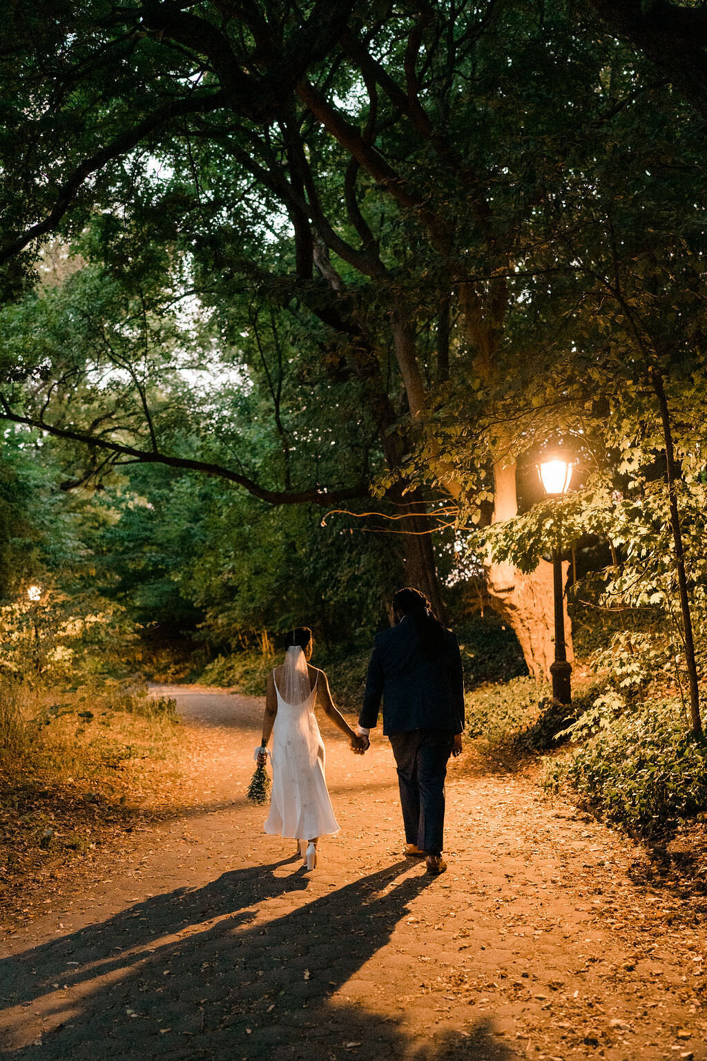 a bride and a groom holding hands and walking on a path in a park