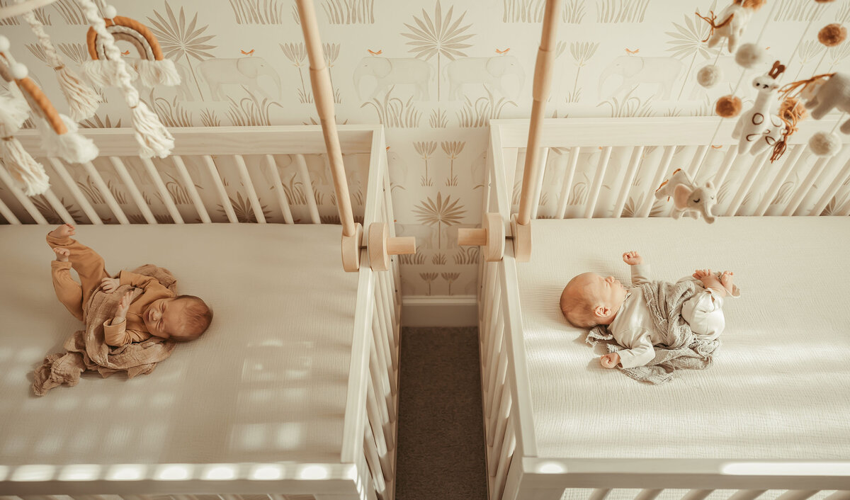 twin newborn babies sleeping side by side in their cribs