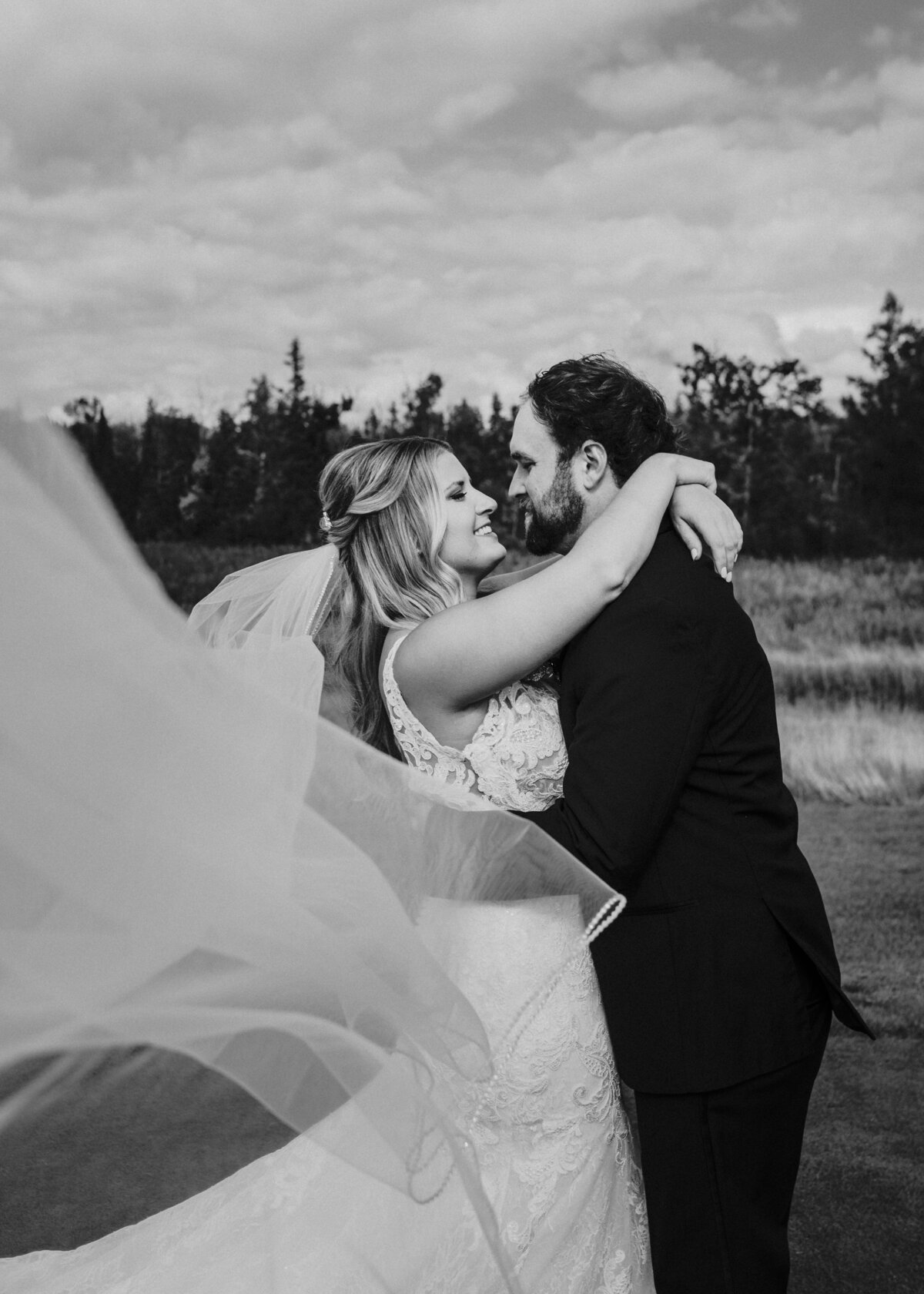 A tender moment captured in monochrome where a newlywed couple lovingly embrace, with the bride's veil caught in the gentle breeze taken by Jen Jarmuzek Photography Minneapolis wedding photographer