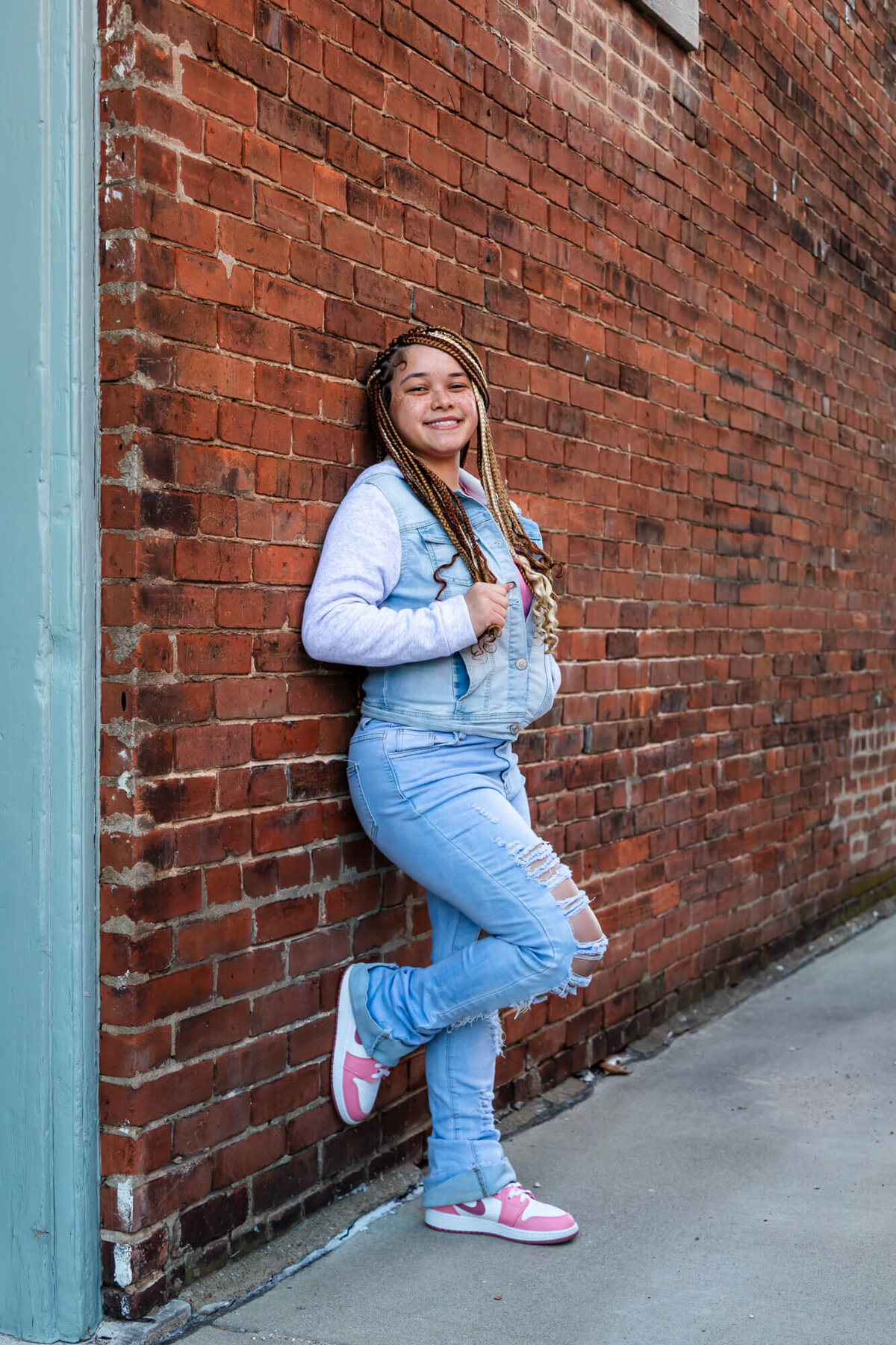 Urban senior picture of a girl with beautiful braids wearing a light wash denim outfit with pink and white Nike's. Captured by Springfield, MO senior photographer Dynae Levingston.