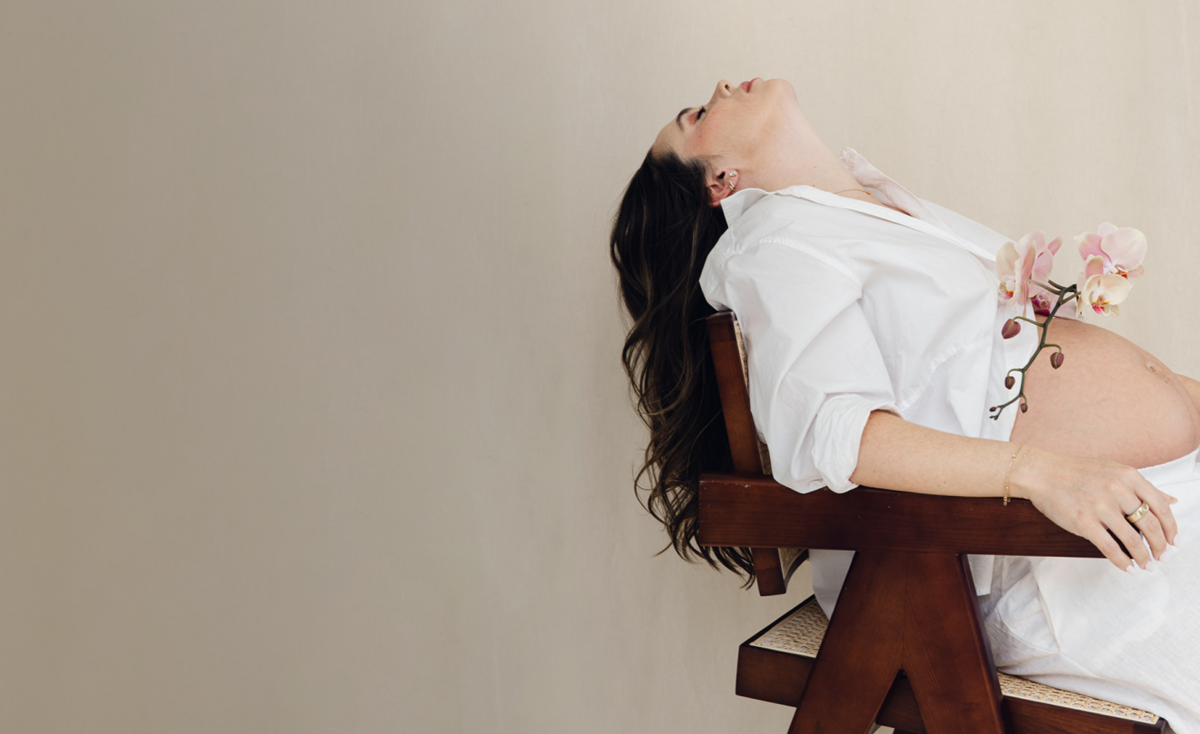 pregnant woman leaning back on a dark wooden chair with an orchid 
