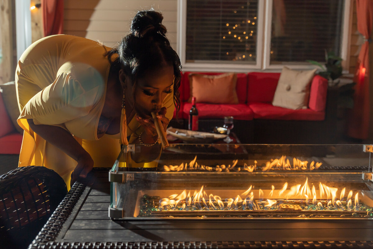 50th milestone birthday photoshoot woman wearing mustard colored romper sitting by outdoor firepit