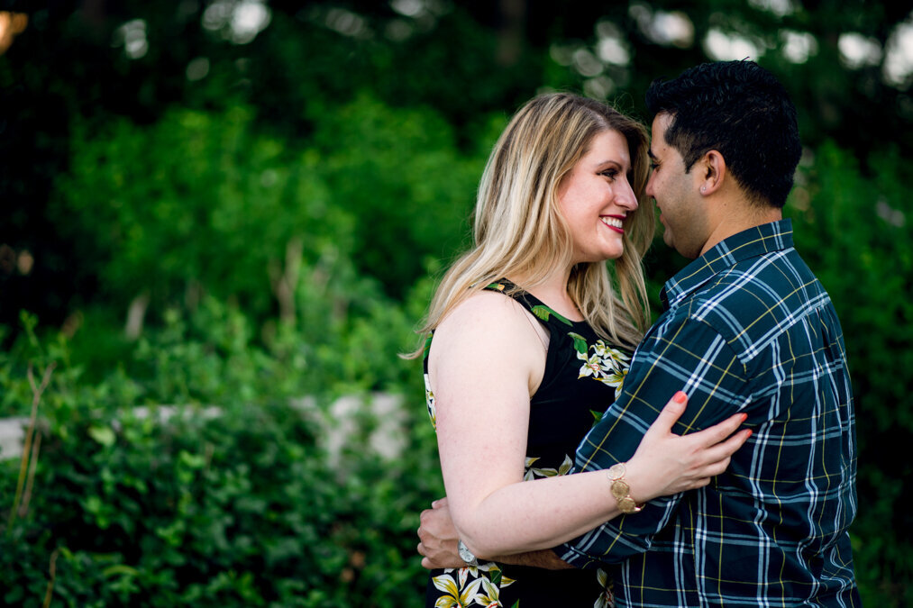 An engaged couple embracing in front of bushes.