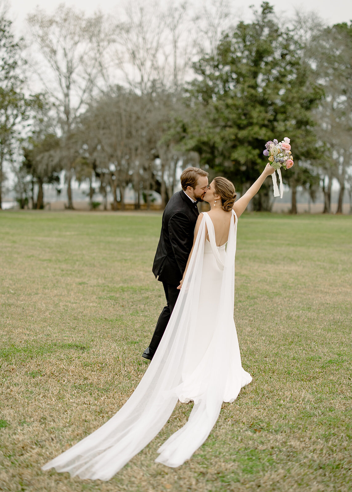 Bride and groom kissing with bouquet in the air and backs to camera