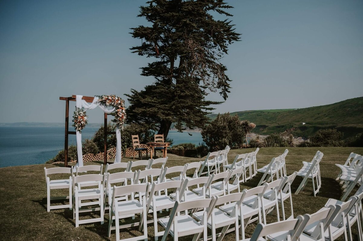 A wedding ceremony set up with white chairs and a view of the sea