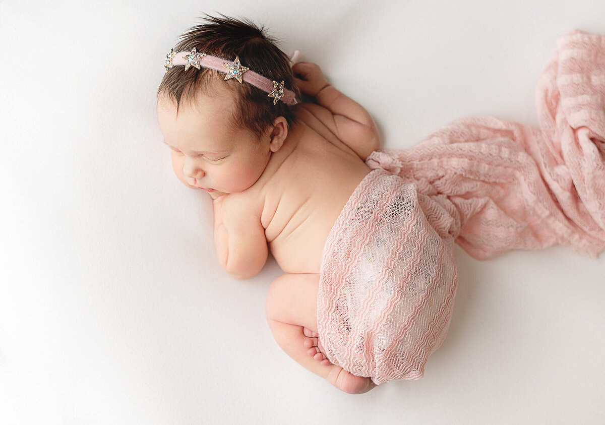 Newborn girl sleeping on a white blanket wrapped in pink.