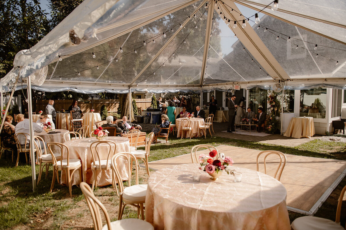A picturesque garden wedding setting with elegant round tables, wooden chairs, and floral centerpieces enhancing the outdoor atmosphere.