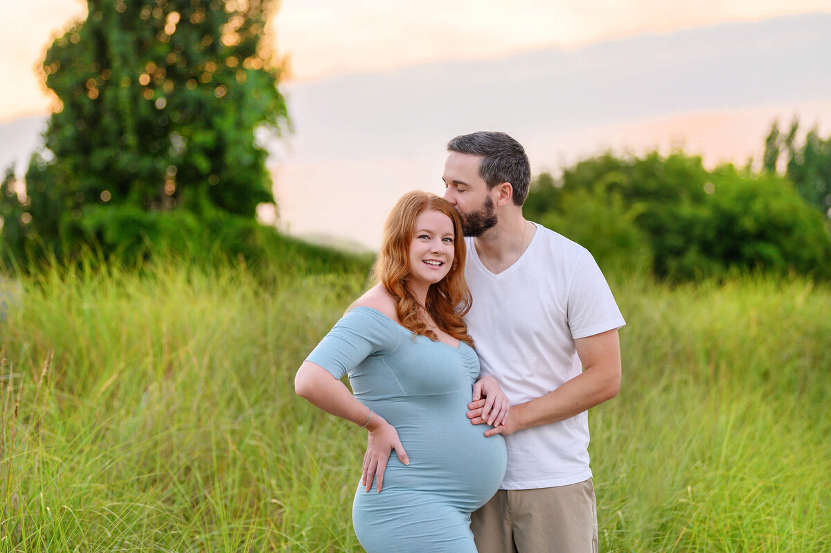 Husband kissing pregnant wife's head and holding her belly for their outdoor maternity photography session in Burlington, Ontario