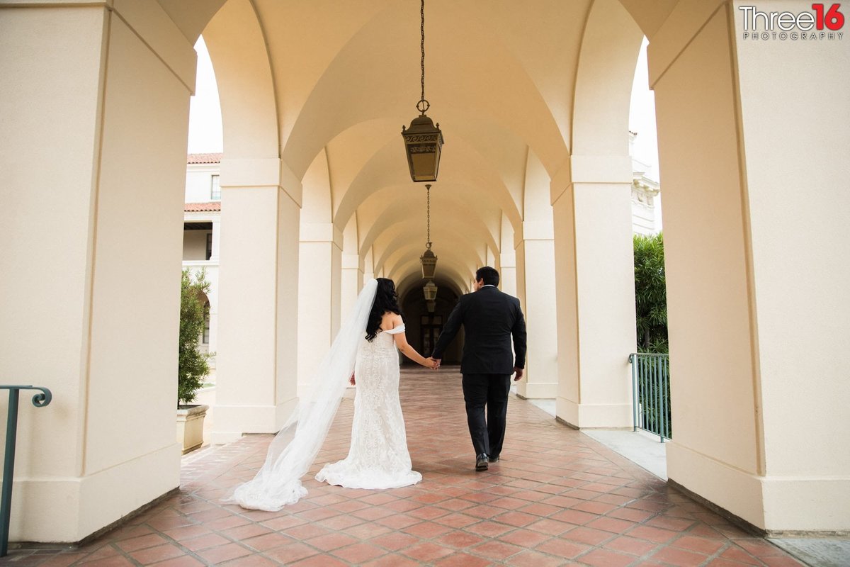 Bride and Groom walk hand in hand along a Pasadena City Hall outdoor corridor