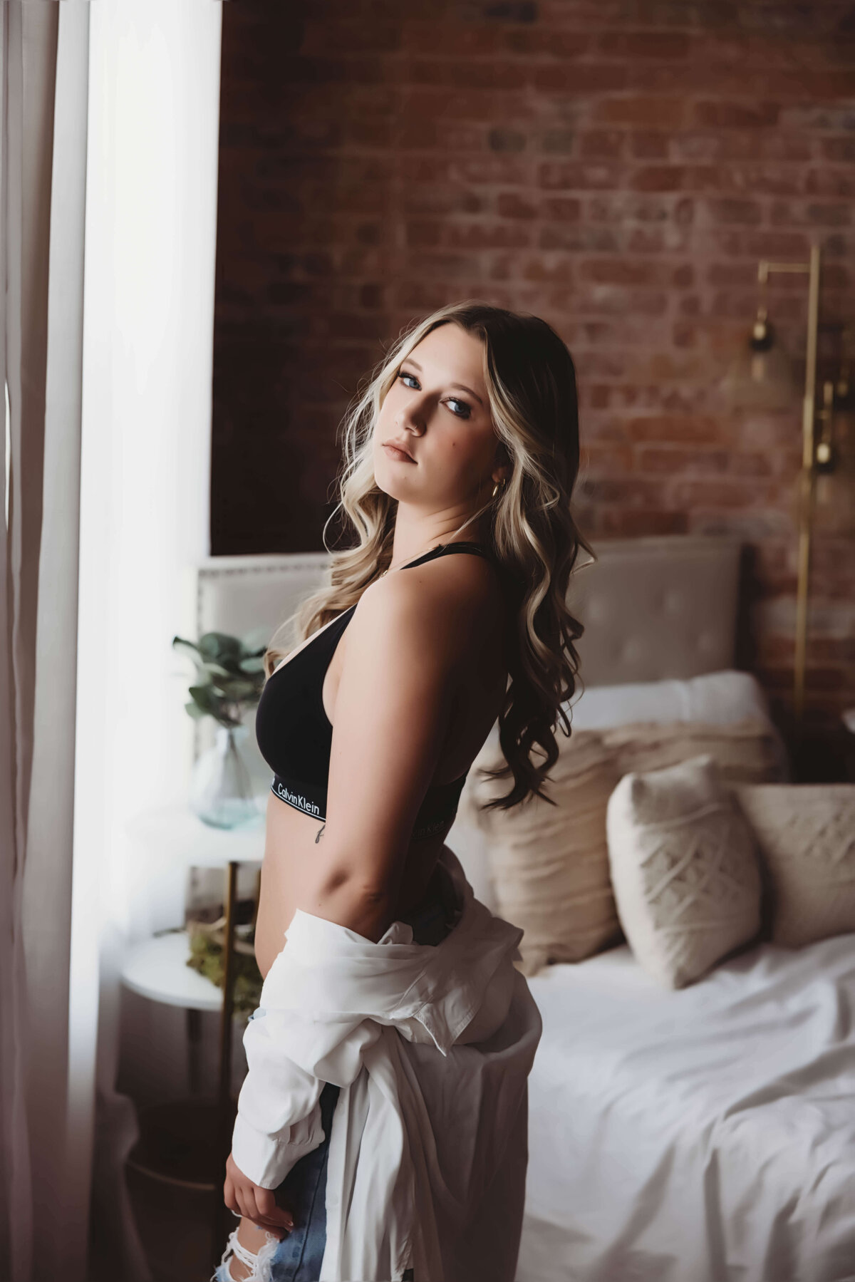 Woman standing by window in Calvin Klein and jeans for boudoir session with Reva Davis photography