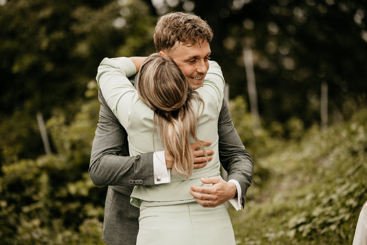 Een spontane knuffel tussen een bruid en gast, omringd door een serene groene omgeving, vastgelegd door IMAI Wedding.