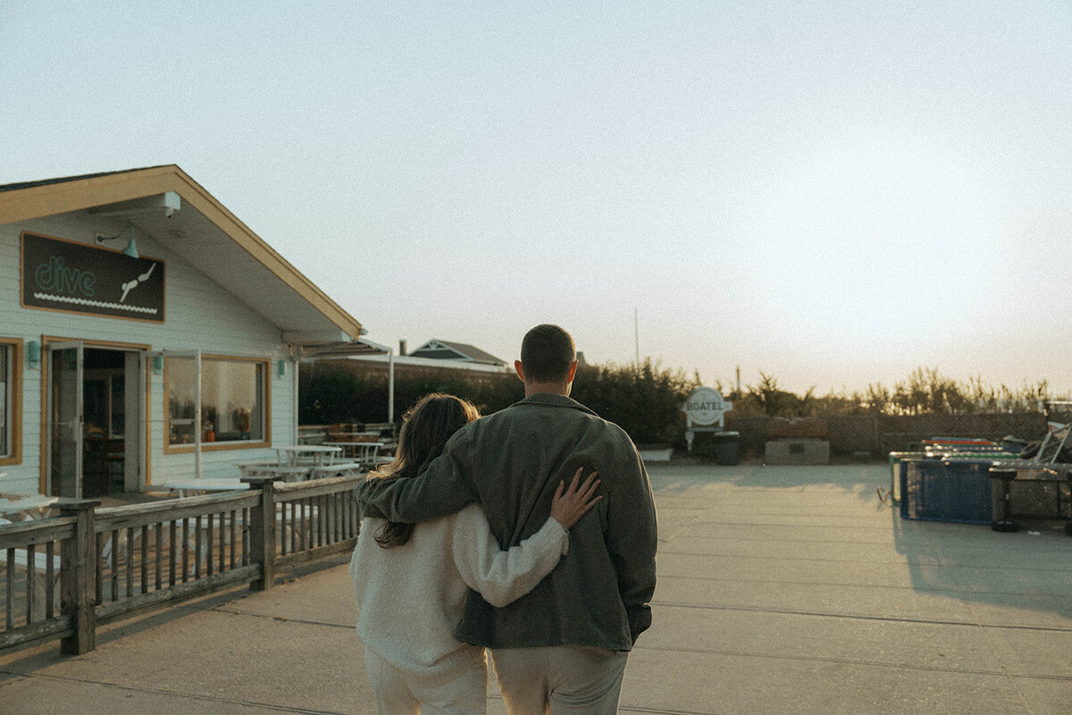 couple walking with arms around each other during beach engagement photos, captured by Elsie Goodman, an NYC engagement and couples photographer