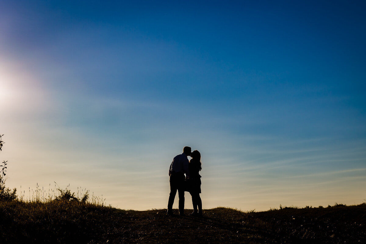 Silhouette of couple embracing on hill with blue and yellow sky