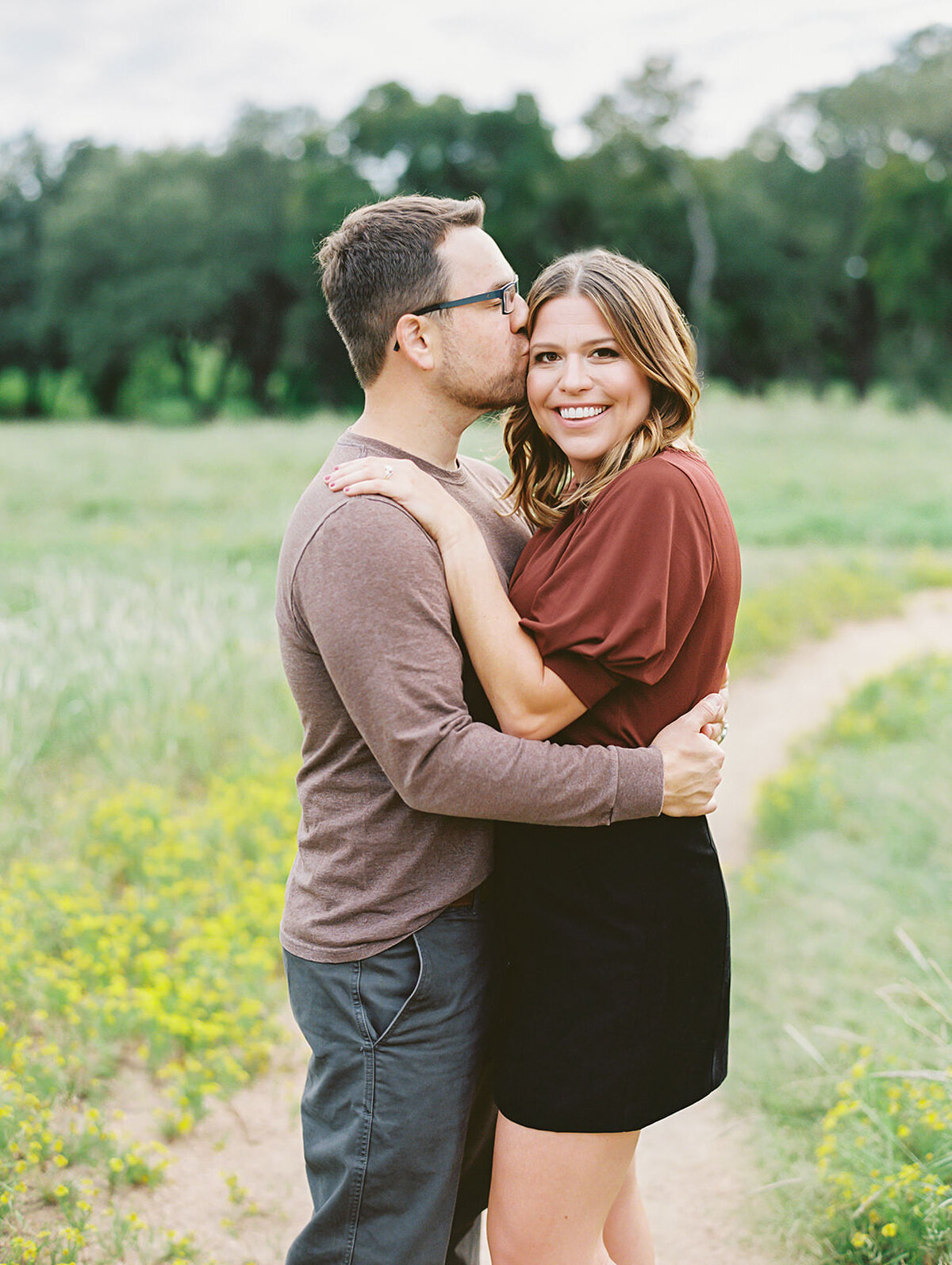 Groom kisses bride on the cheek while wearing a fall color palette for engagement photos