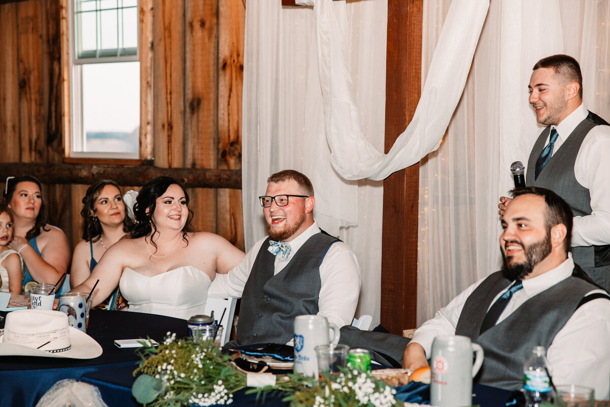A best man gives a toast as the newlyweds laugh at head table