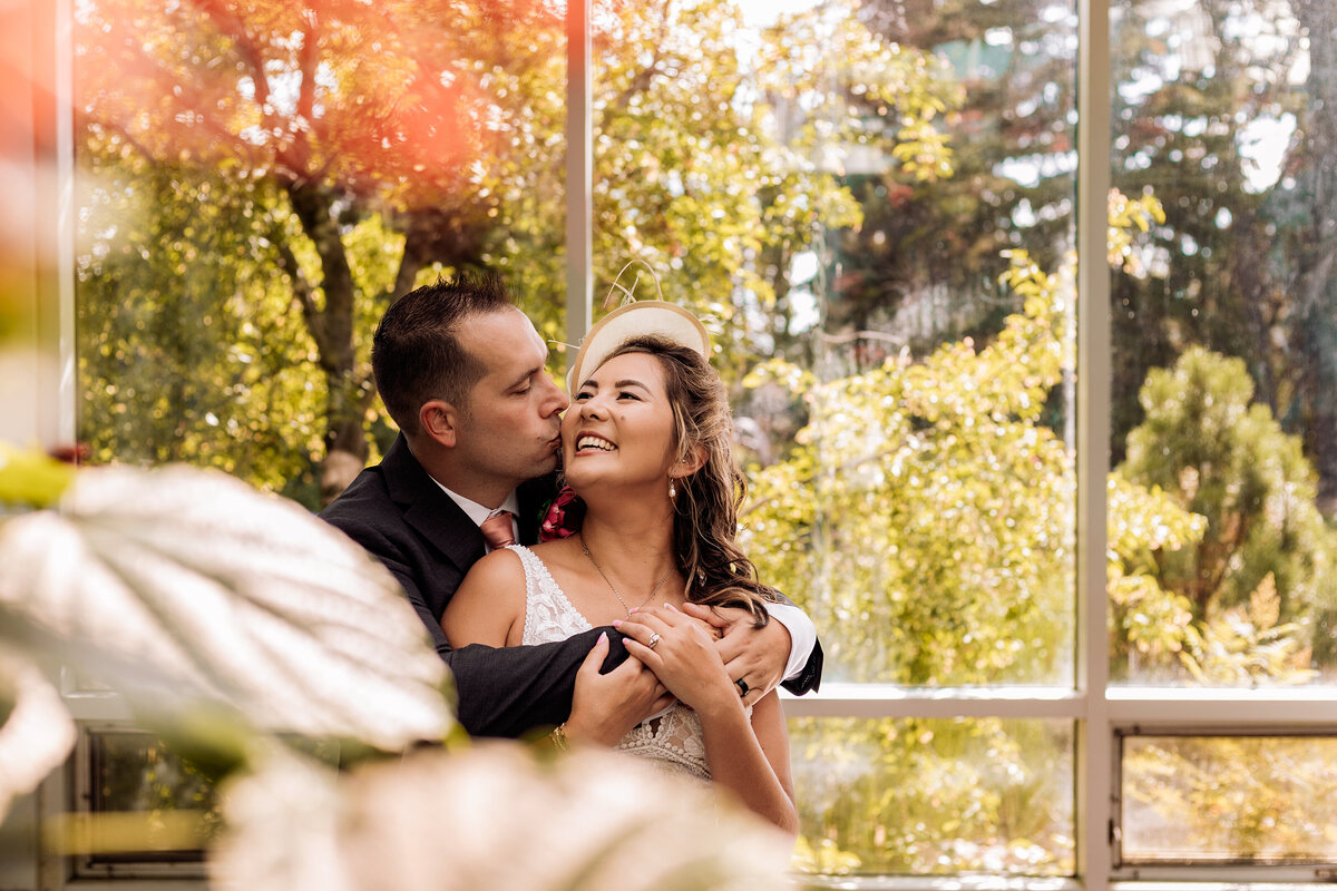 Groom kisses bride on the cheek at the Calgary Zoo Enmax Conservatory