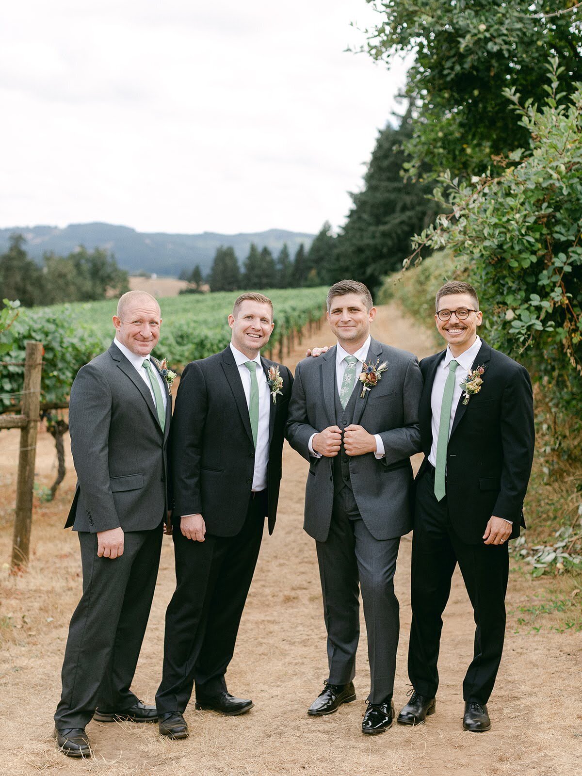 A groom and his groomsmen wearing boutonnieres in a winery row.