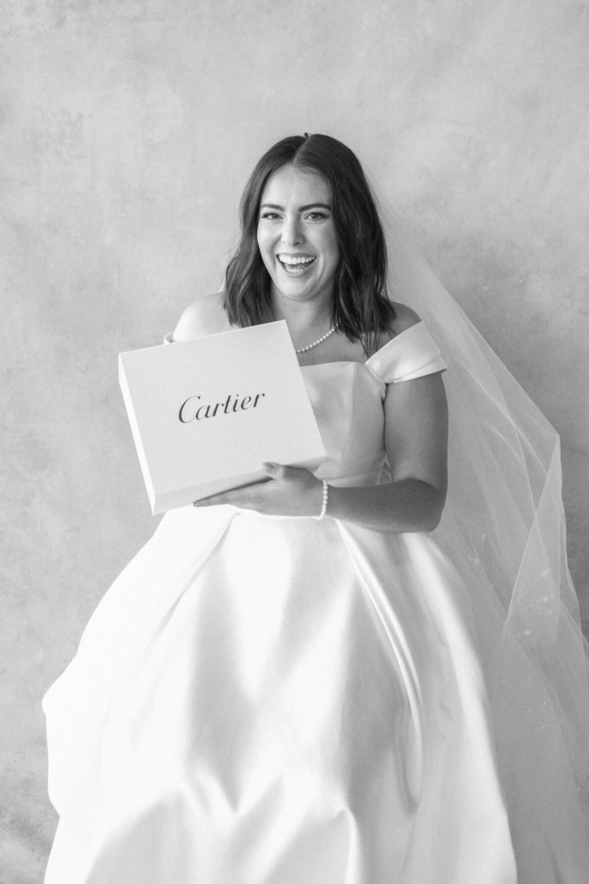 Bride in her wedding gown holds a Cartier box and smiles