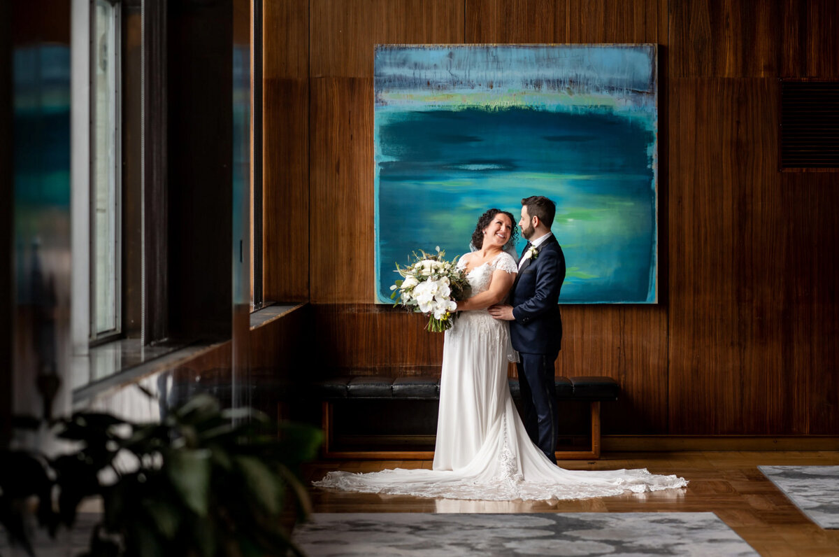 Bride and groom, looking at each other in front of a blue painting inside of the Loews hotel in Philadelphia, PA after their first look