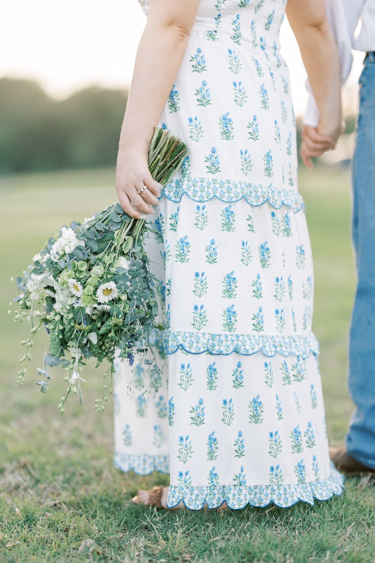close up of an engaged woman wearing a blue and white floral patterned dress and holding greenery
