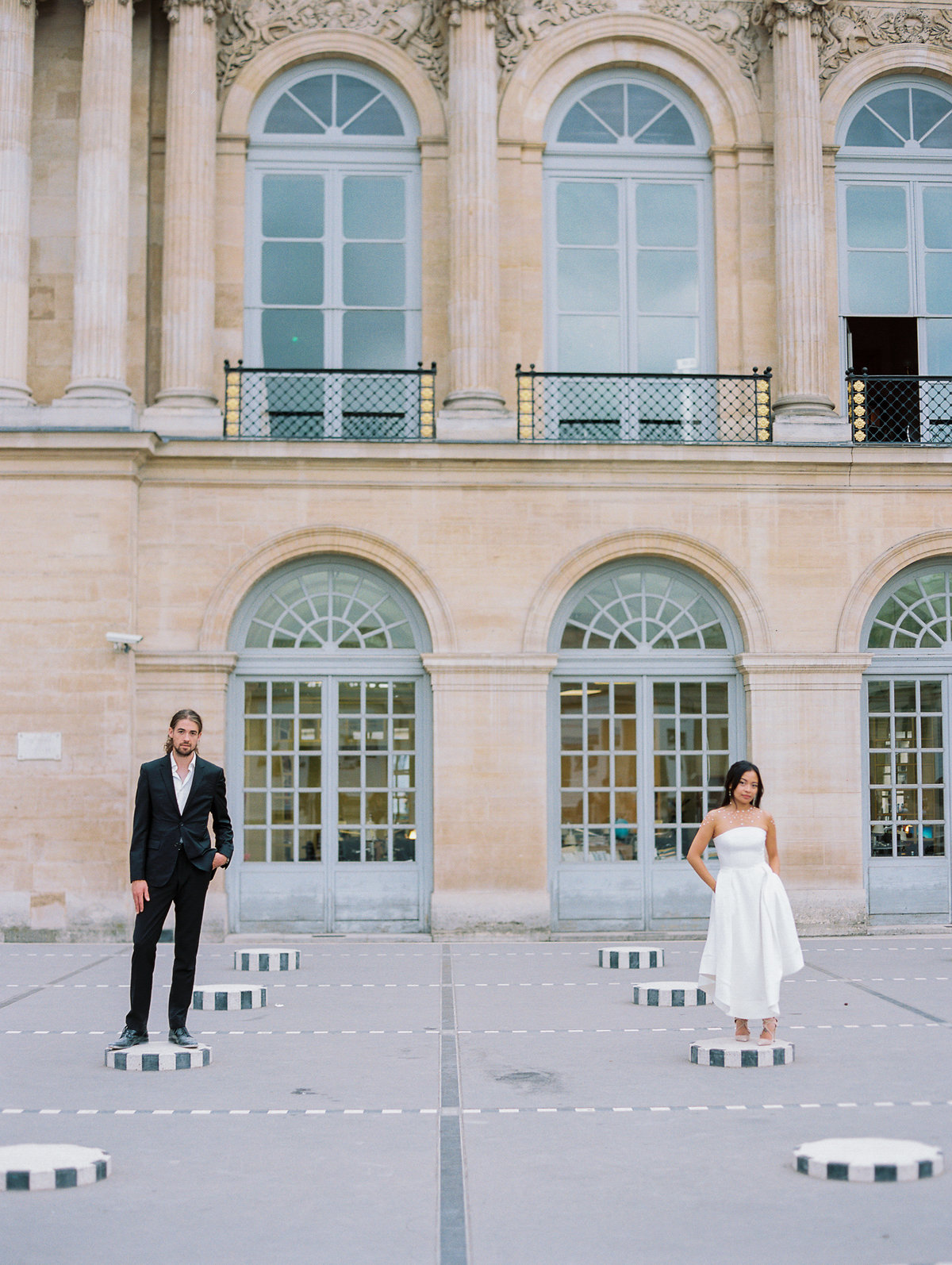 couple staning apart on back and white pillars. bride with short midid dress and groom with black suit