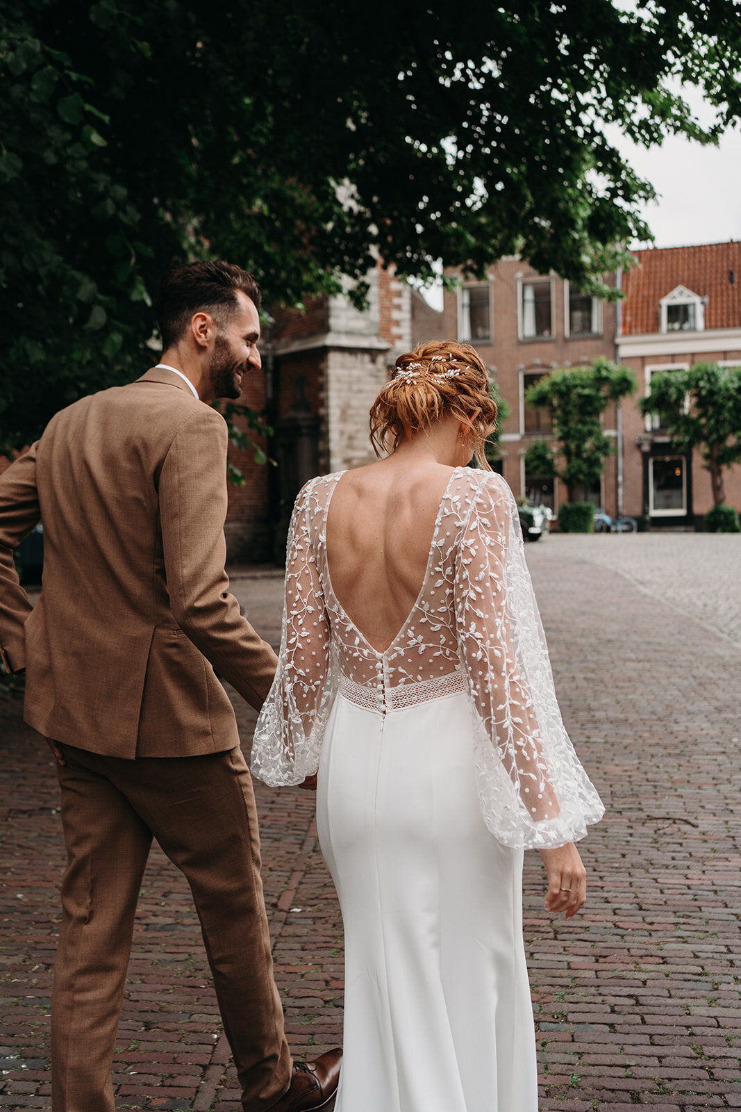 Het bruidspaar loopt hand in hand door de straten van Leiden. De bruid draagt een prachtige klassieke jurk en de bruidegom een stijlvol bruin pak