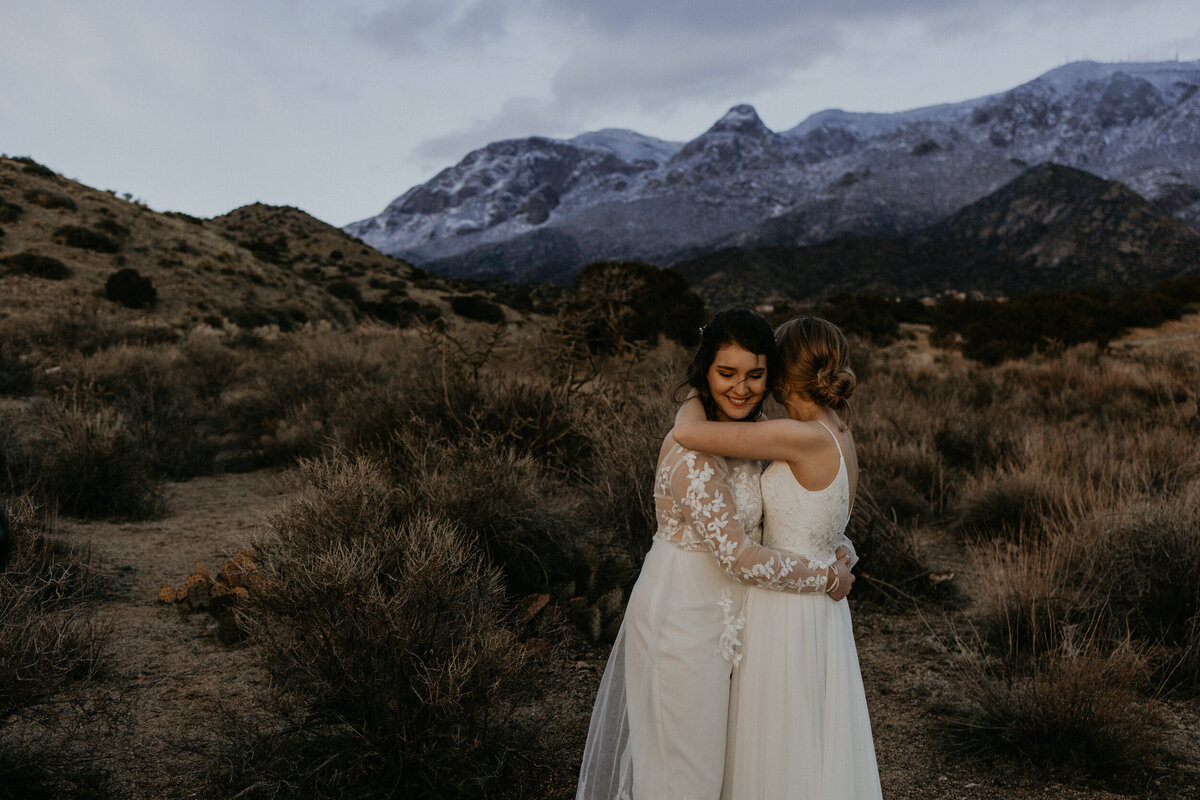 newlywed brides holding each other in front of the Sandia mountains in Albuquerque, New Mexico
