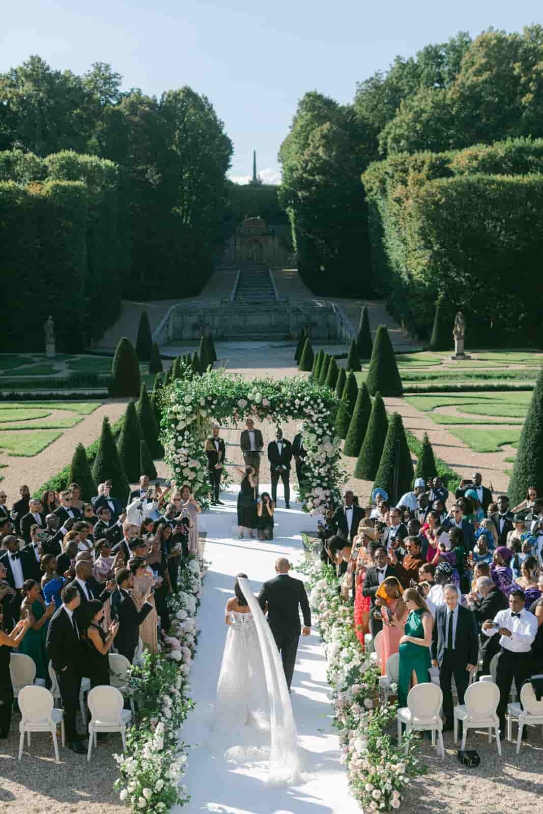 Bride walking down the aisle under a floral arch in a French garden ceremony, documented by Paris wedding photographer Thomas Raboteur