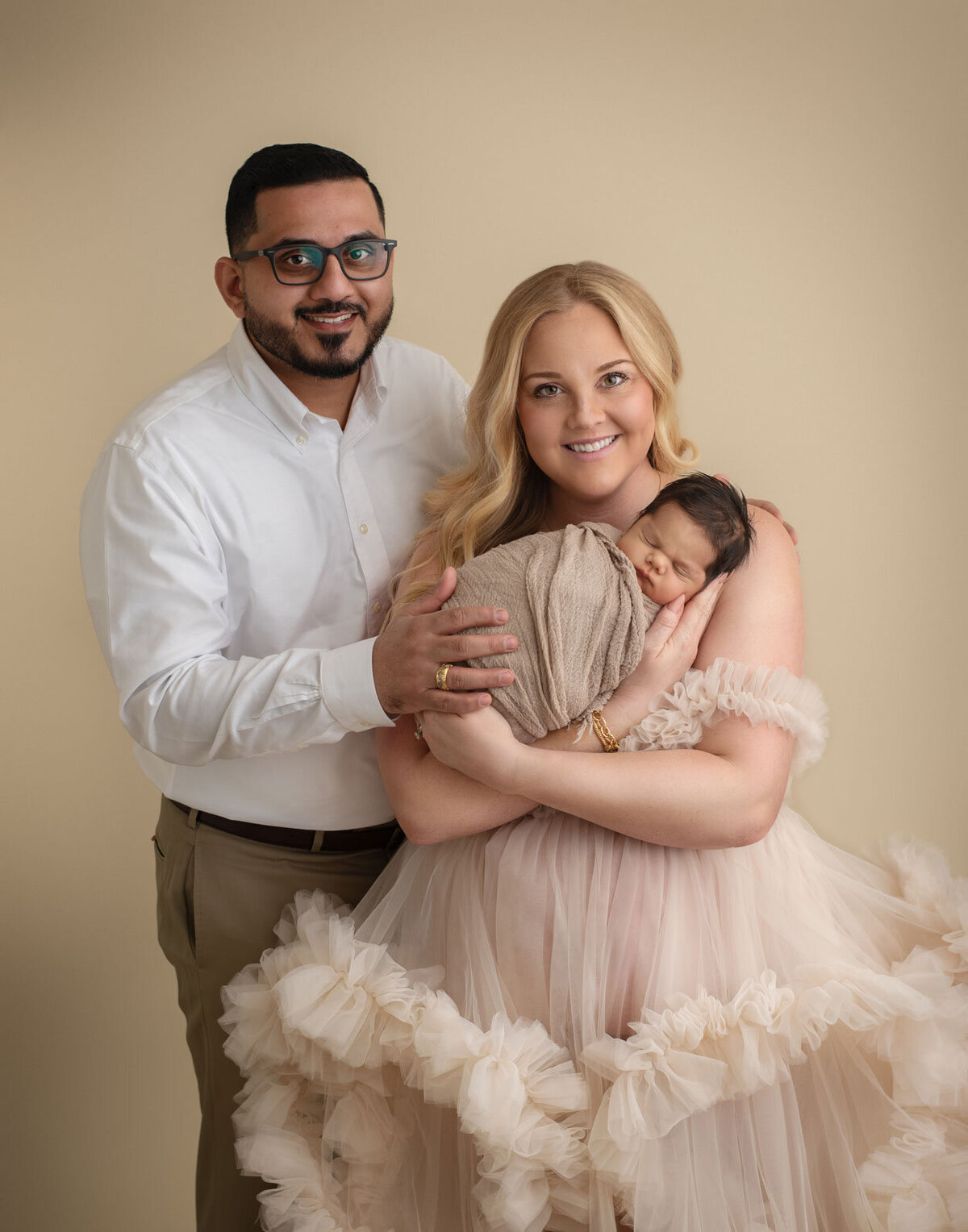 mom and dad dressed up and holding newborn with neutral background