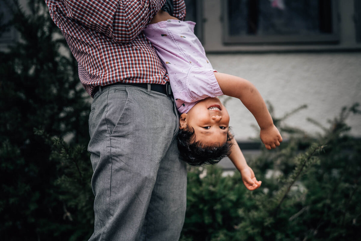 A young boy laughs as he is dangled upside down by his father during an at home family photoshoot with Kate Simpson Photography in Minneapolis.