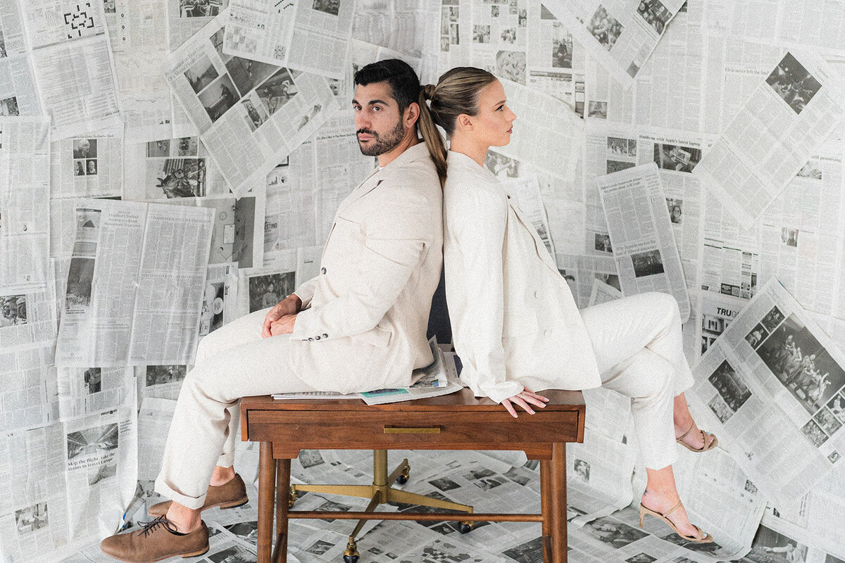 A couple sits back to back in front of newspapers
