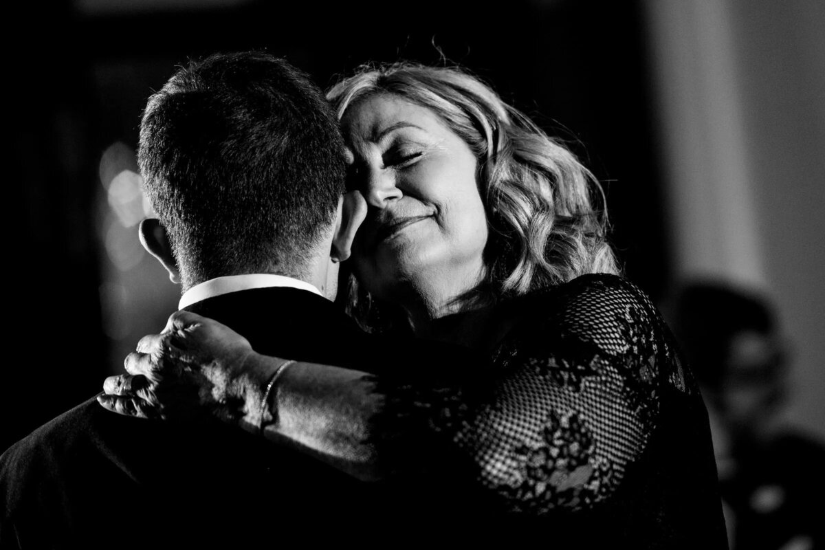 An intimate black and white image of a woman in a lace dress embracing a man in a suit, her face showing contentment and love.