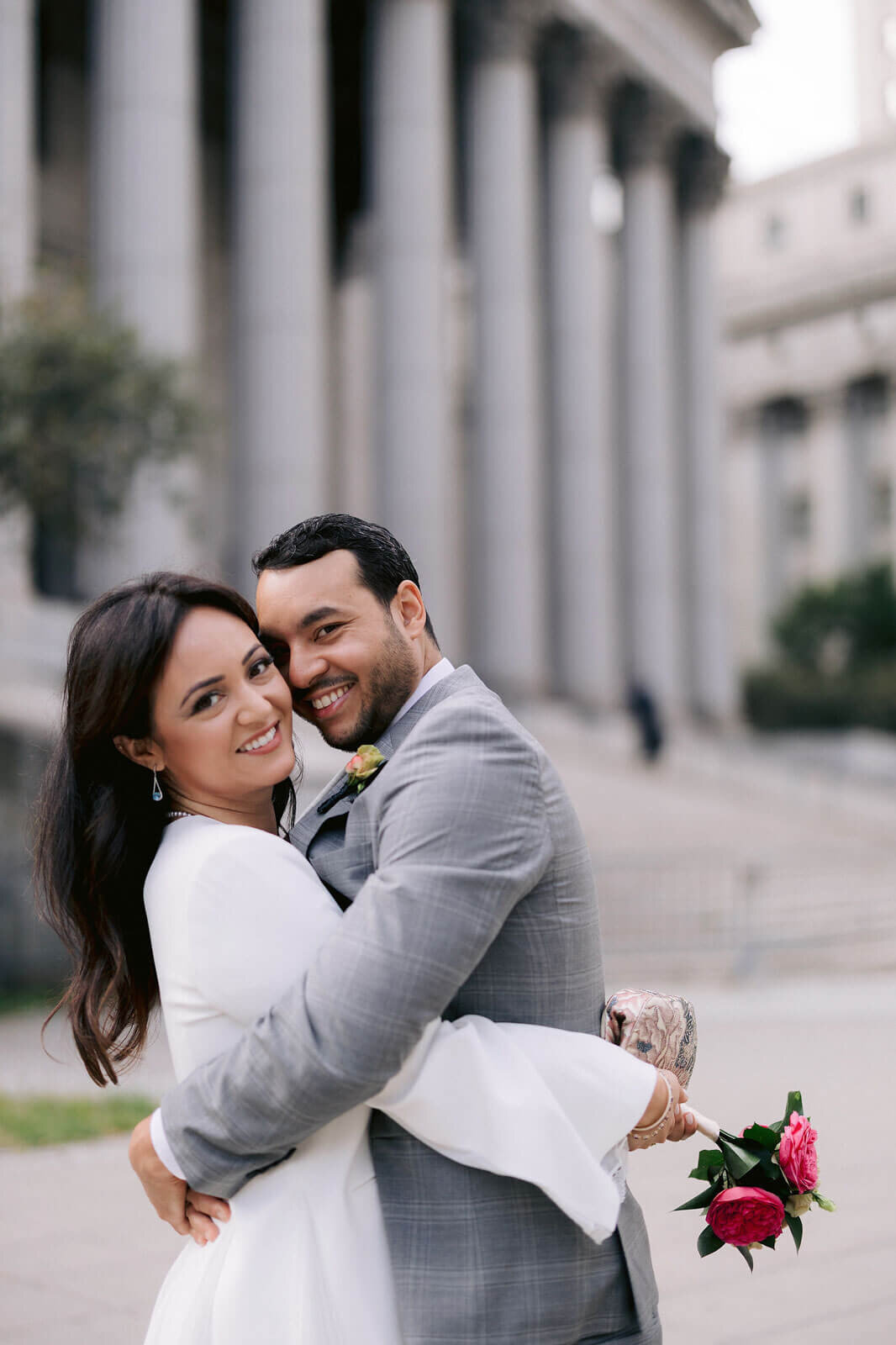 The bride and groom are hugging each other outside New York City Hall. Image by Jenny Fu Studio