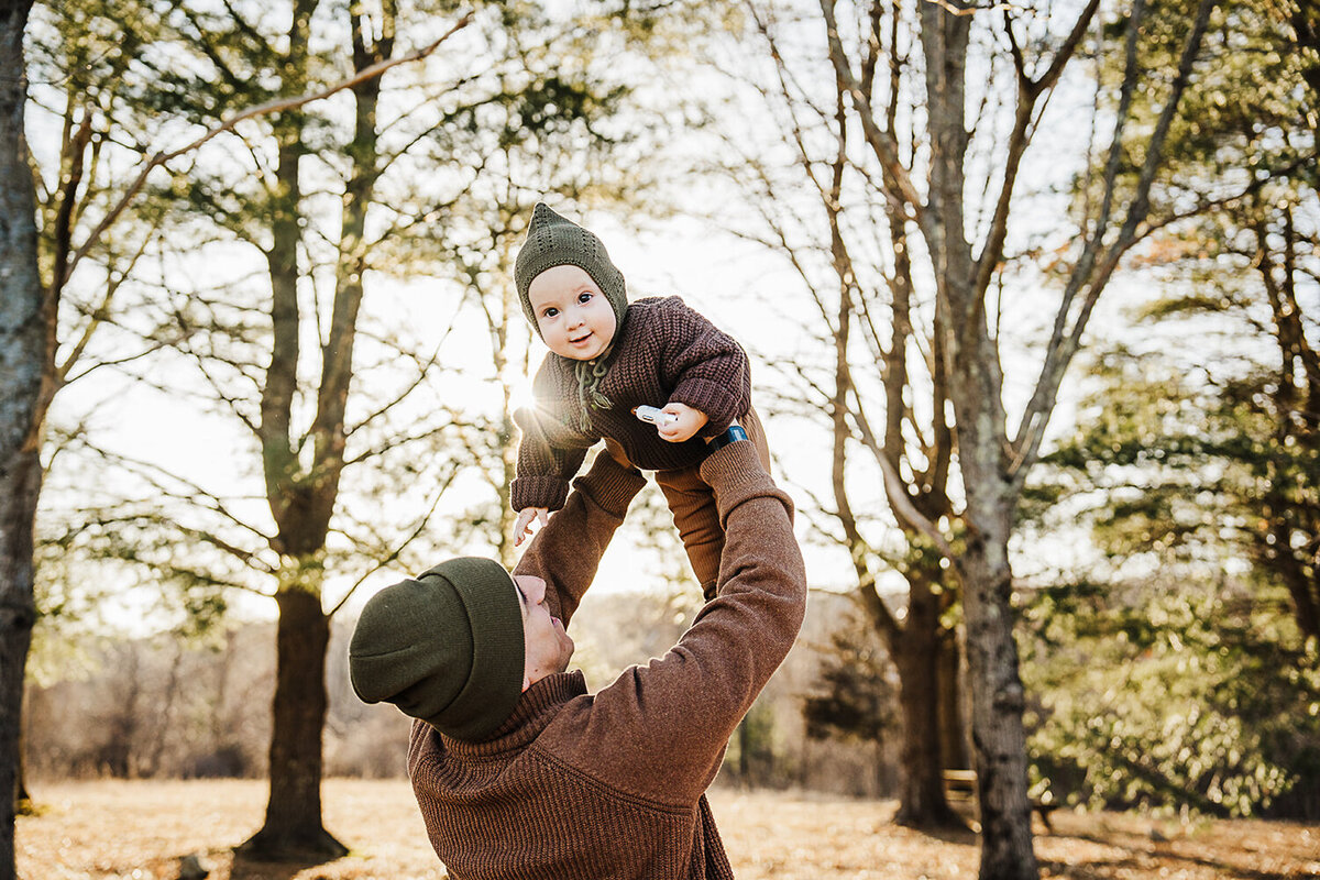dad holds baby son with hat in air in winter