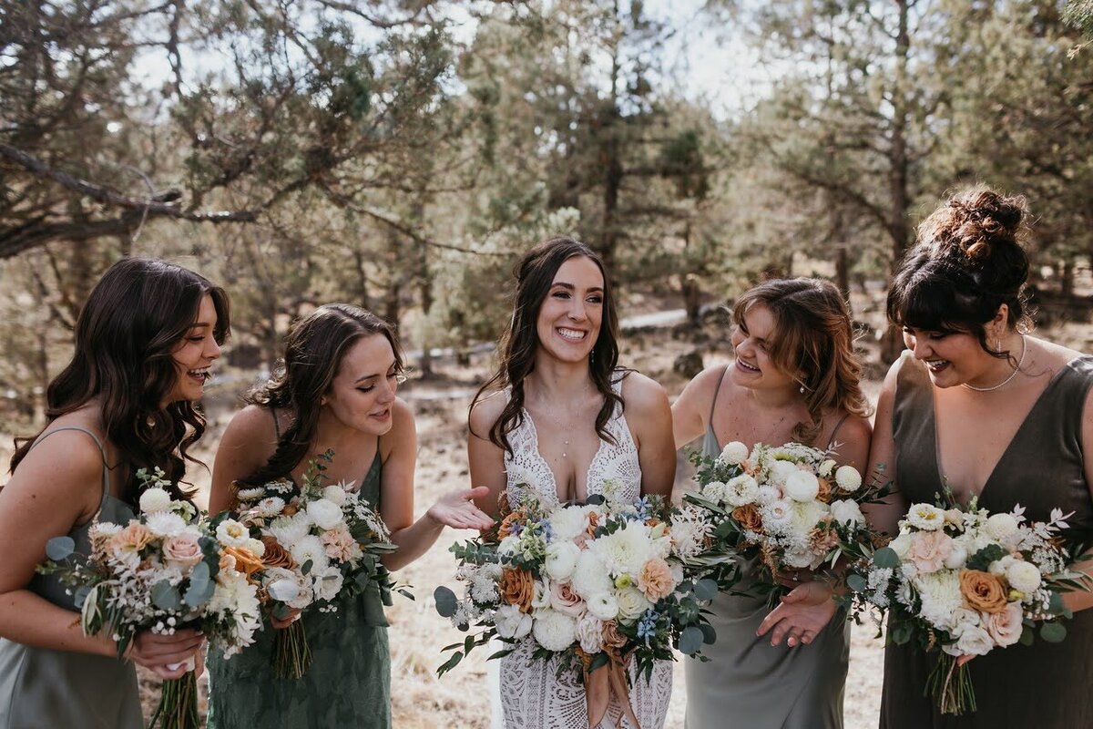 A bride and her bridesmaids hold their bouquets and smile while admiring the bouquets.
