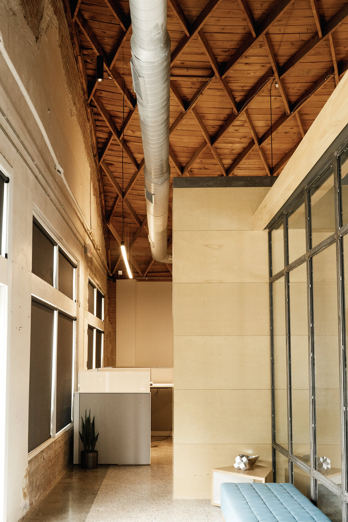 renovated office building interior with wood ceiling, spiral duct, black mullions storefront windows into meeting room and concrete floors