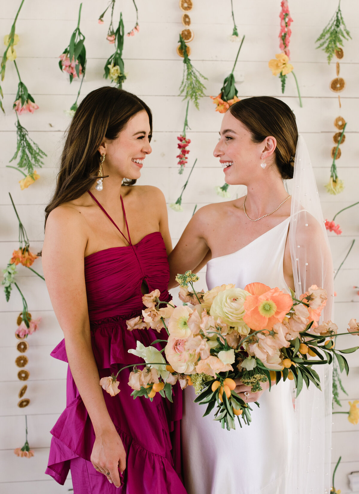 Bride with wedding guest in purple dress with yellow and peach florals surrounding them