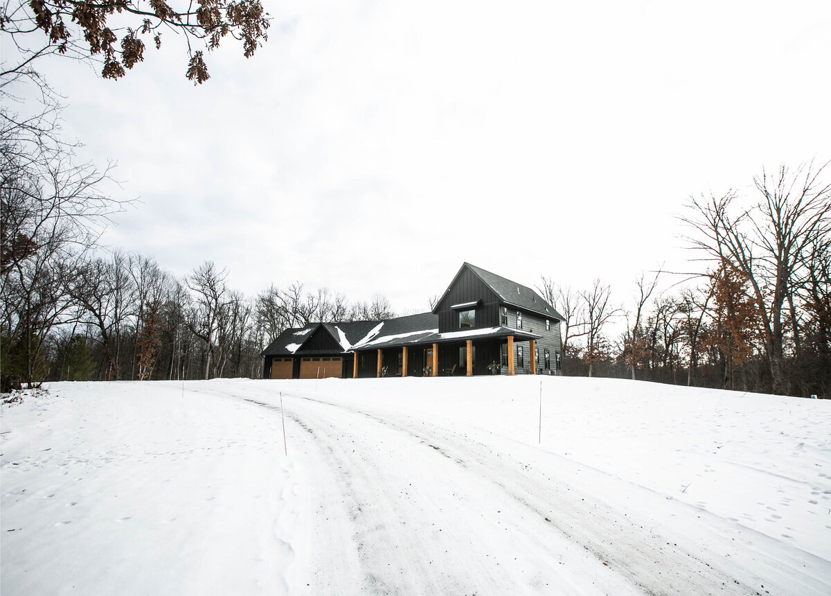 Exterior view of custom home in Elk River, Minnesota with black siding, wood details and front porch built by Cornerstone Custom Builds