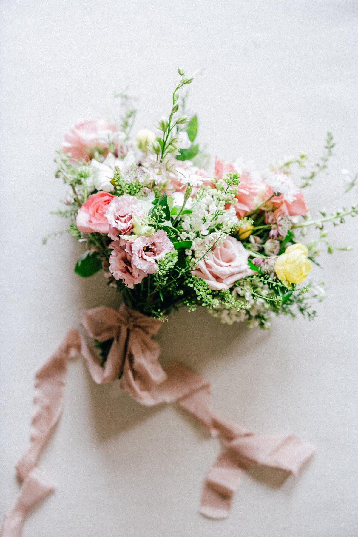 A delicate bouquet of pink and white flowers with greenery and a trailing ribbon against a white background.
