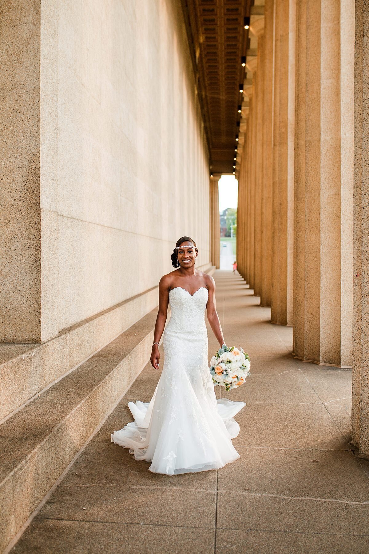 Elegant African American bride holding a peach, white and orange bouquet wearing a strapless flowing wedding gown and a rhinestone headband at The Parthenon in Nashville, TN